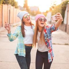 Wall Mural - Two cheerful girls takes pictures of themselves on the mobile phone.