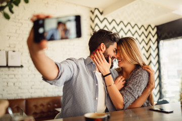 Wall Mural - Young fashion lover couple at beginning of love story. Handsome man taking selfie with pretty woman at fashion coffee bar. Relationship concept with nice boyfriend and girlfriend.