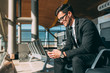 © DavidPrado - Young business man sitting on the phone with the suitcase at the airport waiting for the flight