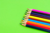 Fototapeta Tęcza - Row of colorful wooden pencils on background of green paper