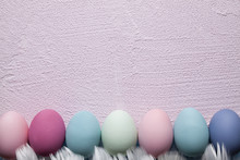 Colored Easter Eggs And Feathers On Pink Plastered Wall Background
