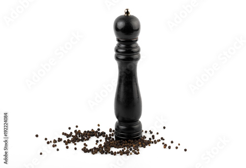 Fotomural pepper mill with black peppercorns on white background.