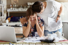 People, family troubles concept. Unhappy young woman being in bad mood, looks desperately down, faces some problems with preparing business documents, her best friend tries to help and encourage