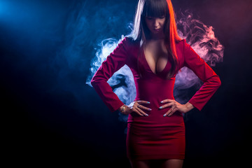 Young dark-haired woman in a red dress posing against a background of red and  blue smoke from a vape on a black isolated background