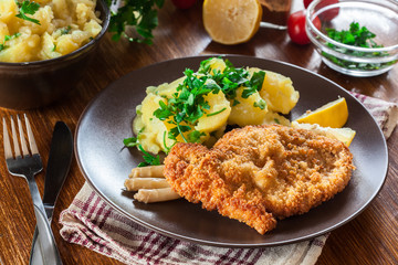 Canvas Print - Homemade breaded viennese schnitzel with potato salad and asparagus on a plate