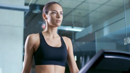 Wall Mural - beautiful woman athlete wearing sport bra, walks on a treadmill, uses touchscreen option for optimal