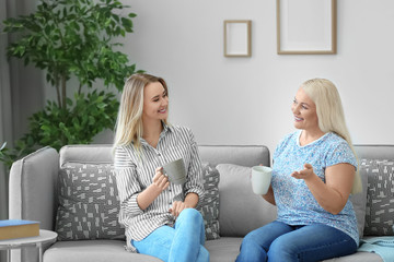 Canvas Print - Young daughter and mother drinking coffee on sofa at home