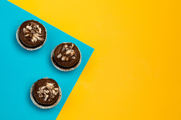 Wall Mural - chocolate cupcakes on a color yellow-blue background decorated with chocolate shaving