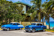 Zwei amerikanischer blau weisse Oldtimer mit weissem Dach parken unter Palmen am Strand von Varadero Kuba - HDR - Serie Cuba Reportage