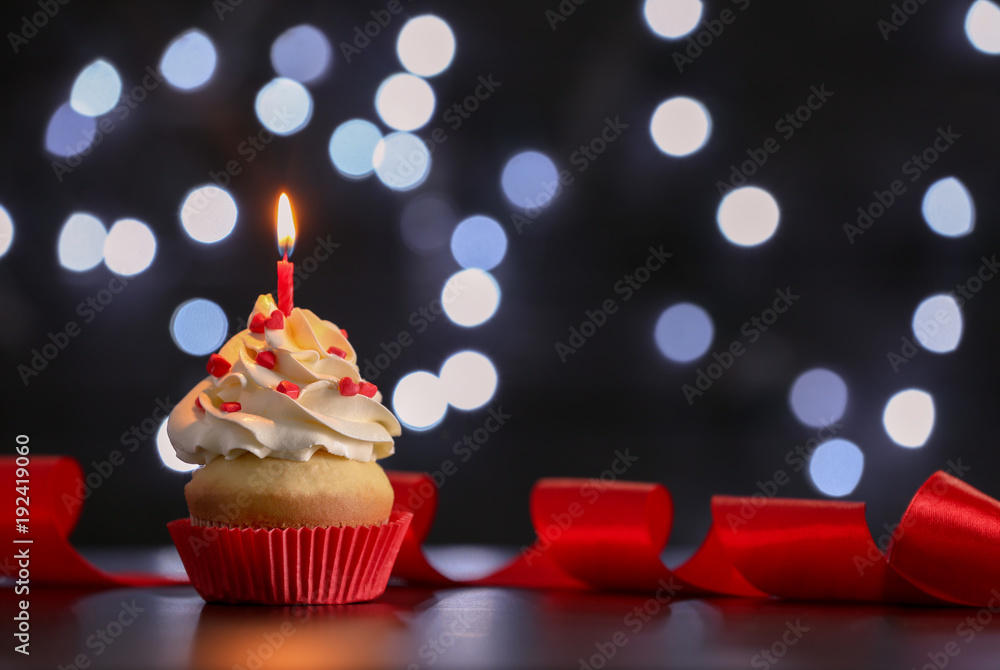 Birthday cupcake with candle on table against blurred lights