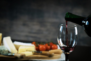 Wall Mural - Pouring red wine into the glass against wooden background