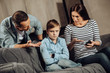 Clear explanation. Strict young parents telling their son about the drawbacks of binge-playing on the phone while the boy, scolding him, while the boy looking offended