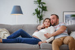 © Sergey - Image of happy pregnant woman and man sitting on gray sofa