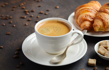 Cup of fresh coffee with croissants on dark background, selective focus