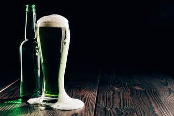 glass and bottle of green beer with foam on table, st patricks day concept