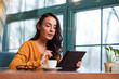 © zinkevych - Innovative technology. Musing focused attractive woman sitting at table while using tablet and looking down