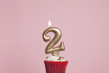 Number 2 gold candle in a cupcake against a pastel pink background