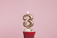 Number 3 Gold Candle In A Cupcake Against A Pastel Pink Background