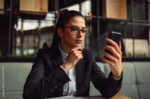Close-up of young businesswoman in cafeteria looking at screen of her mobile phone Poster