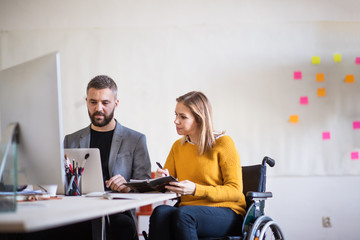 Two business people with wheelchair in the office.