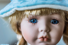 Close-up Of Beautiful Porcelain Doll With Blond Hair And Blue Eyes, Sky Blue Vintage Dress And Leather Shoes. Little Princess Games.