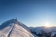 Skitourengeher erreicht Gipfelkreuz im Winter während Sonnenuntergang