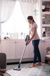 The smiling young woman is vacuuming in the room at home