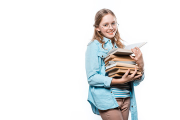 beautiful teenage girl in eyeglasses holding stack of books and smiling at camera isolated on white