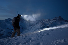 Brave Night Explorer Climbs On High Snowy Mountains And Lights The Way With A Headlamp. Extreme Expedition. Ski Tour. Snowboarder Commit Climb On Winter Slope. Backcountry