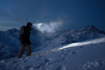 Brave night explorer climbs on high snowy mountains and lights the way with a headlamp. Extreme expedition. Ski tour. Snowboarder commit climb on winter slope. Backcountry