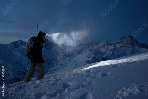 Foto  Brave night explorer climbs on high snowy mountains and lights the way with a headlamp