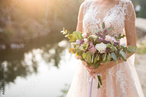 Cuadros en Lienzo The bride in a beige wedding dress holding a lush bridal bouquet of lilac roses and a lot of greenery