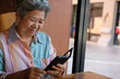 © 88studio - elder woman holding mobile phone in garden. elderly female texting message, using app with smartphone at home. senior use cellphone to connect with social network