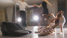 Blurred Professional Man And Woman Dancing Latin Dance In Costumes In Studio, Two Pairs Ballroom Shoes In The Foreground
