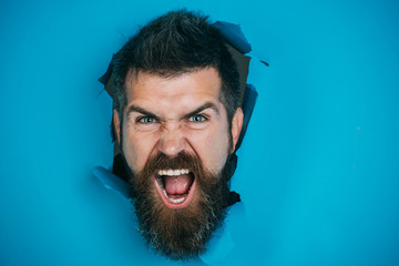 Wall Mural - View of male face through hole in blue paper. Angry bearded man making hole in paper. Bearded man looking through hole.