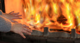 Fototapeta Miasto - Ogień w kominku, kobieta grzeje dłonie.