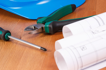 Rolls of electrical drawings, protective helmet and work tools for engineer jobs lying on desk