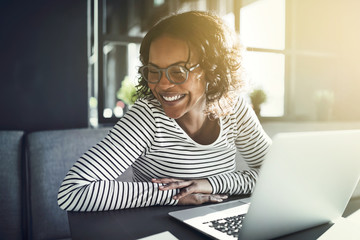 Wall Mural - Young African woman laughing while browsing online with a laptop