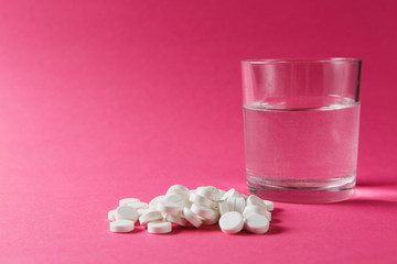 Medication pile white round tablets arranged abstract on pink rose color background. Aspirin, glass water pills for design. Health treatment choice healthy lifestyle concept. Copy space advertisement.