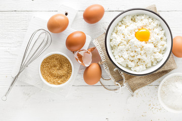 Canvas Print - Culinary background with ingredients for cooking, cottage cheese, baking flour, sugar and eggs on white wooden rustic table, top view