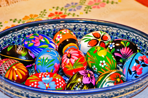 Fotografering Colorful Hand Painted Wooden Easter Eggs in a Ceramic Bowl on a cloth with a needlepoint flower design