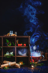 Wall Mural - Wooden case with a collection of magical items, steaming tea cup and scrolls with spells on a dark background. Golden glitter, stars and magical pixie dust on a dark background.