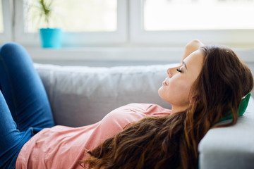 Attractive young woman relaxing on sofa at home with eyes closed