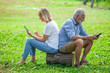 Elderly couple sitting back to back in a park and play mobile phoneand tablet