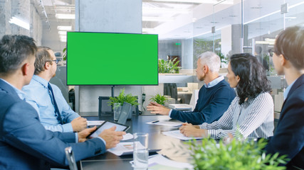 Diverse Group of Successful Business People in the Conference Room with  Green Screen Chroma Key TV on the Wall.  They Work on a Company's Growth, Share Charts and Statistics.