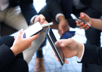 Group of people using smart phones sitting at the meeting, close up on hands.