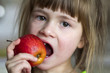 © bilanol - A cute little curly toothless girl smiles and holds a red apple. Portrait of a happy baby eating a red apple. The child loses milk teeth. Healthy food nutrition.