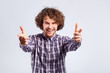A young curly-haired man with a positive emotion points his finger at the gray background.