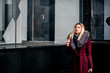 © natasidorova  - Young girl with blonde hair is standing in a burgundy coat and fur collar near the storefront. Fashion shooting