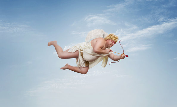 Funny overweight cupid aiming with the arrow of love over clear blue sky with copy space